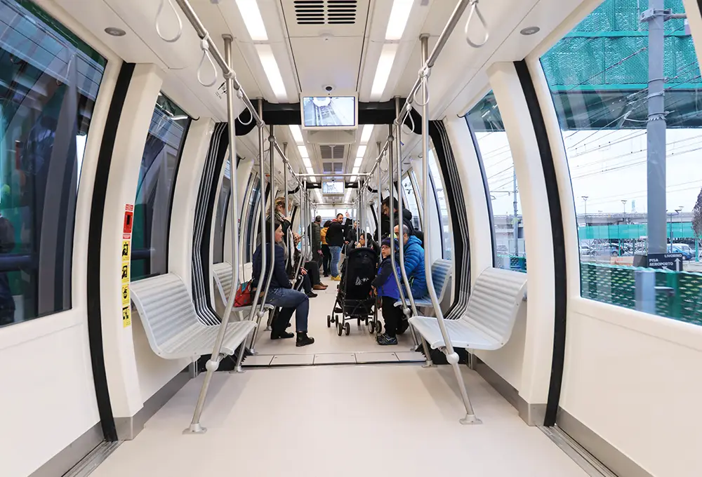 Interno del treno automatico PisaMover con passeggeri seduti e in piedi.