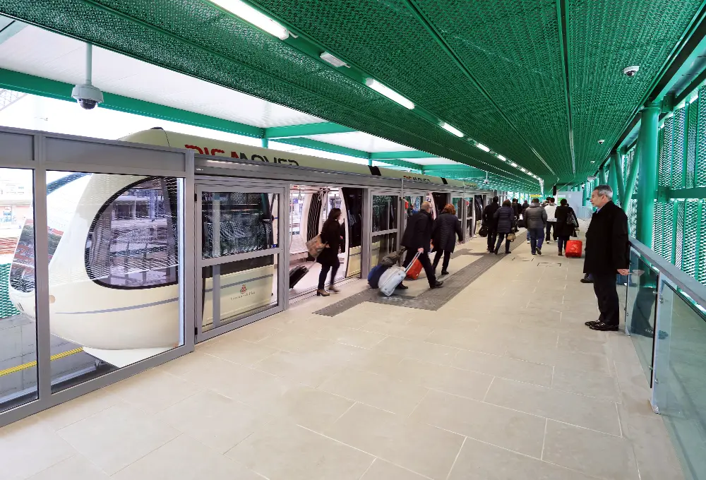Passeggeri con valigie che salgono e scendono dal treno PisaMover alla stazione sopraelevata.